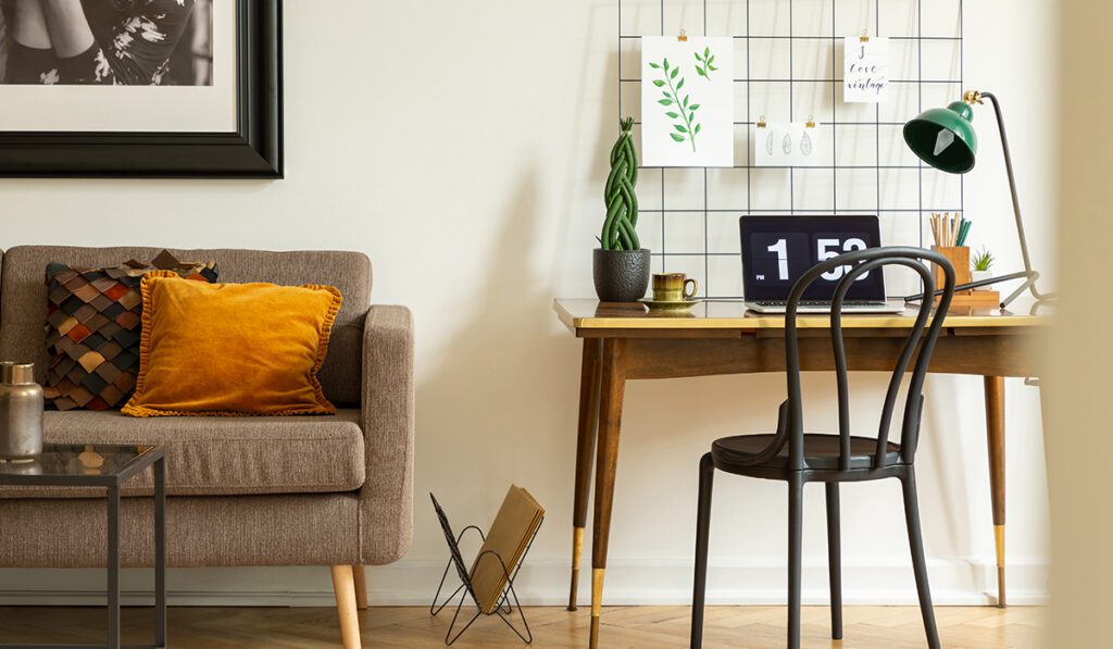 Black chair at desk with laptop and lamp next to couch in white workspace interior. Real photo